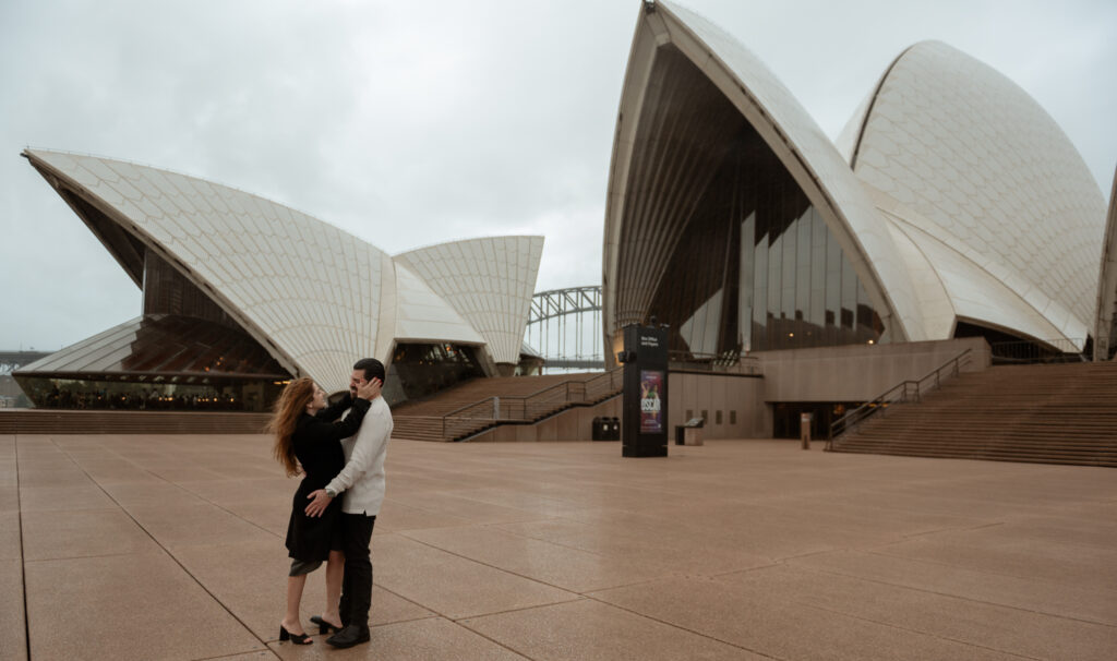 A recent engaged couples is happy cuddling each other at the Sydney Opera House